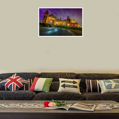 Living room with a dark sofa, assorted pillows, a coffee table with magazines, and a wall photo of an illuminated building.