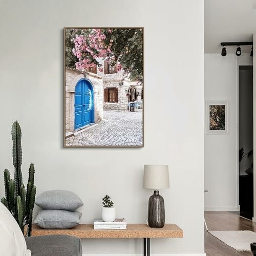 Interior room with wall art of a quaint street scene featuring a blue door and pink flowers.