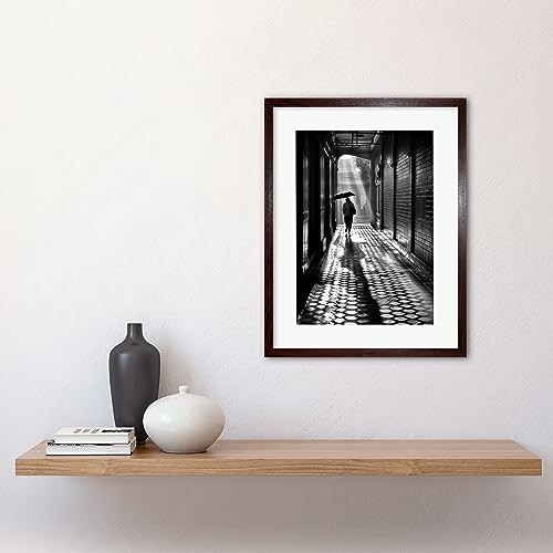 Framed black and white photo on wall above minimalist shelf with vases.